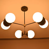 Brass and black ceiling chandelier with six glowing frosted globes, providing warm ambient lighting for modern living spaces.