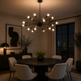 Monaco 18 light black Sputnik chandelier illuminated above a round dining table in a modern evening dining room.