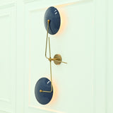 Angled view of Nashville two-light wall sconce showcasing glossy blue disc shades, brass arms, and warm ambient wall illumination.