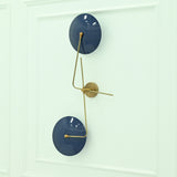 Nashville two-light wall sconce with glossy navy blue dome shades and asymmetrical brass arms mounted on a white paneled wall.