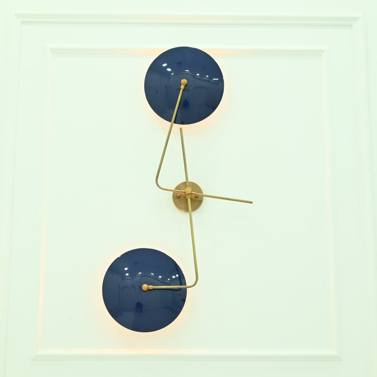 Nashville sculptural wall sconce featuring two navy blue circular shades with warm backlighting and elegant brass geometric detailing.