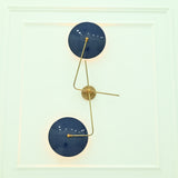 Nashville sculptural wall sconce featuring two navy blue circular shades with warm backlighting and elegant brass geometric detailing.