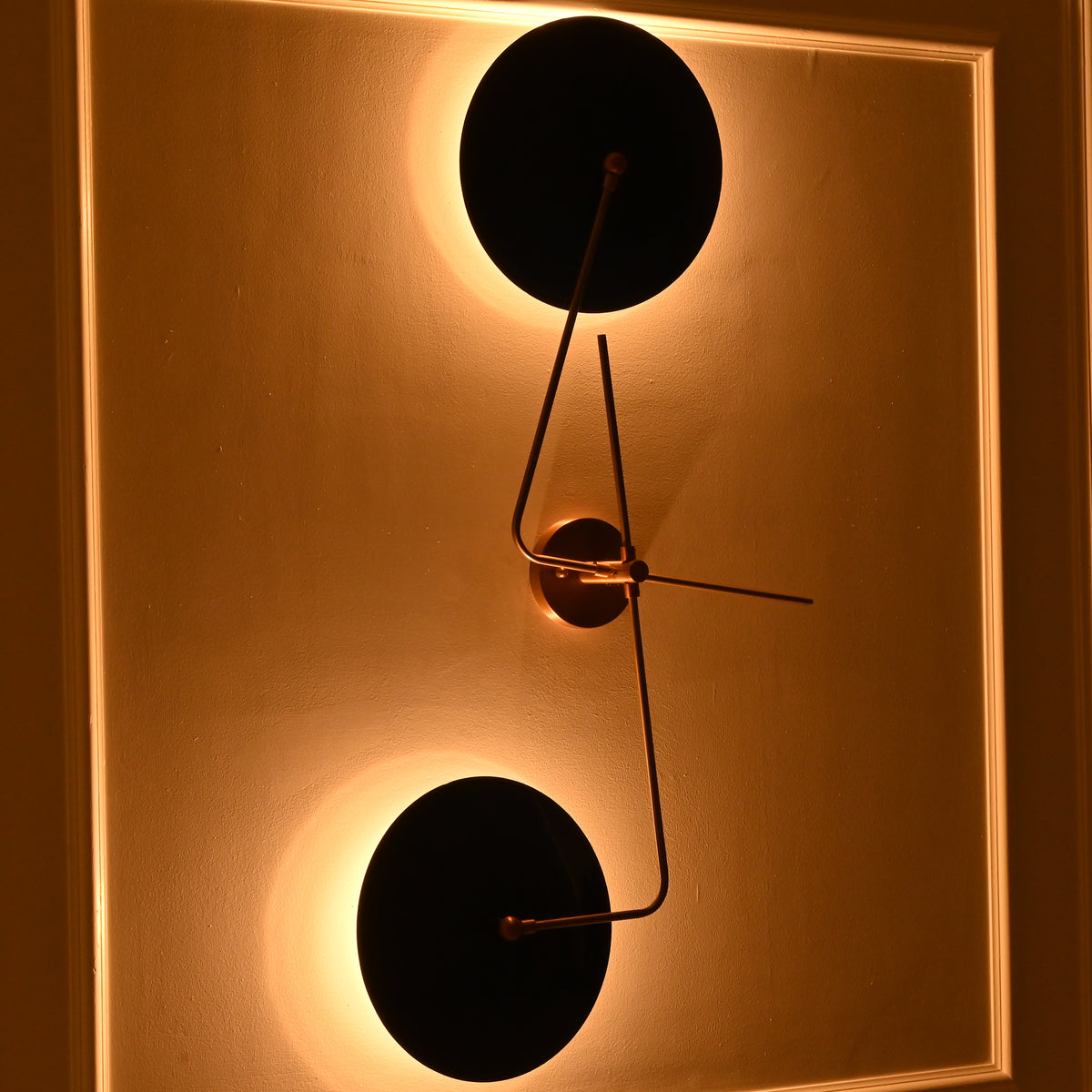 Close-up of Nashville sculptural wall light showcasing intersecting brass arms, two circular metal shades, and warm indirect lighting.