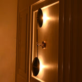 Nashville sculptural two-light wall sconce illuminated at night, casting warm golden light behind its circular shades against a decorative wall.