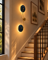 Nashville navy blue dual-disc wall sconce casting warm light along a modern wooden staircase with black railings and neutral walls.