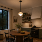 Naxos 1 light dome globe pendant illuminated above a dining table in a warm modern kitchen and dining room interior.