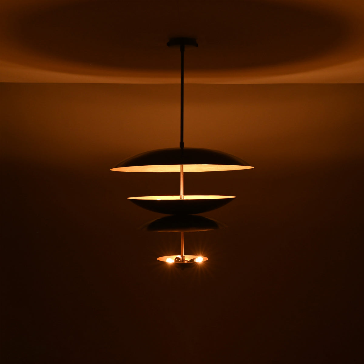 Noir Tiered Disc Chandelier displayed in a dark setting with warm lower bulbs and ambient glow.