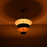 Noir Tiered Disc Chandelier glowing warmly in low light with dramatic ceiling and shade illumination.