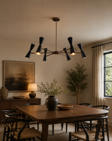 Orion 12-Light Double Cone Chandelier installed above a modern dining table, featuring handcrafted hourglass shades and a Mid-Century Modern brass frame that creates a bold architectural centerpiece.