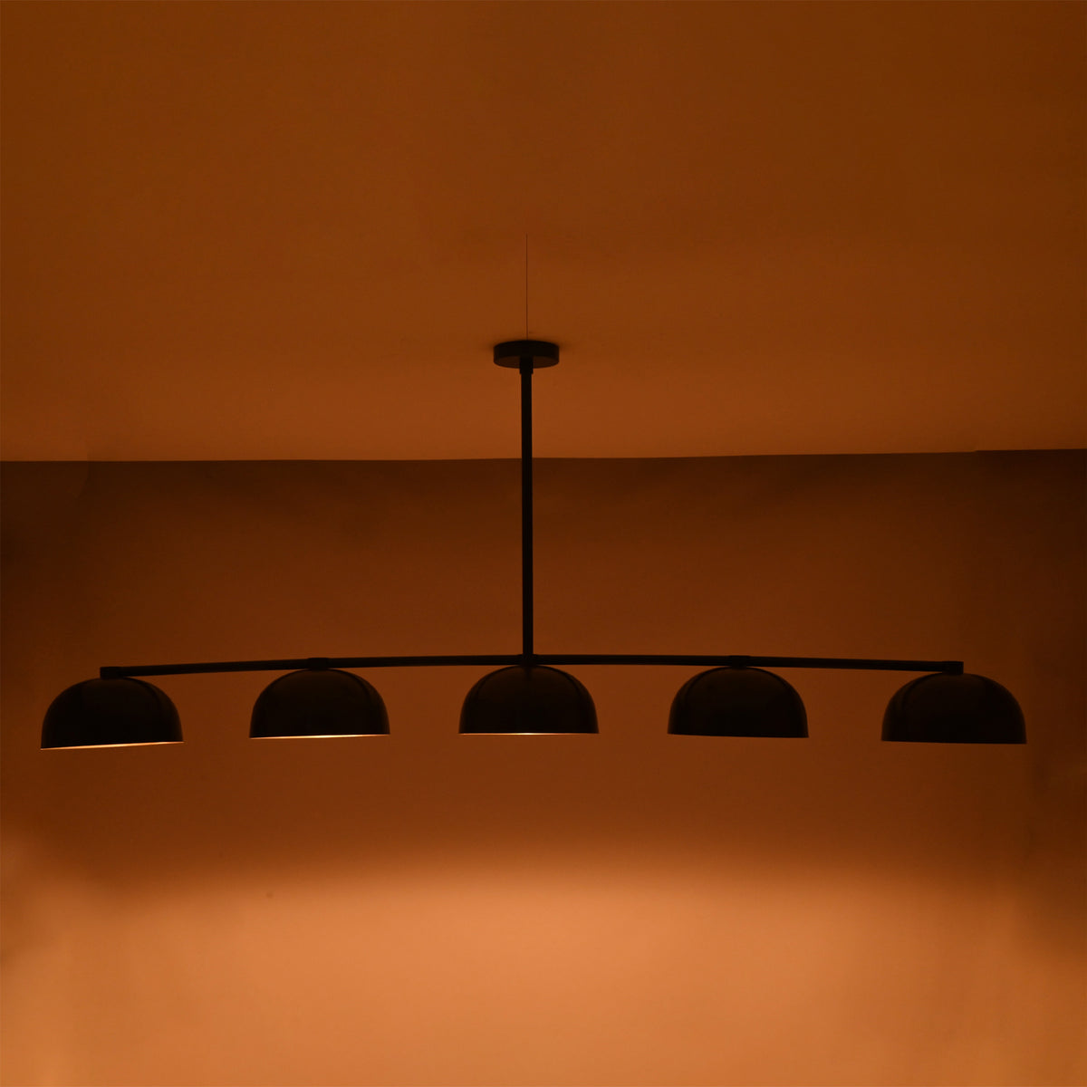 Ambient nighttime view of the Orion 72-inch modern linear chandelier creating balanced downward illumination with warm brass interiors.