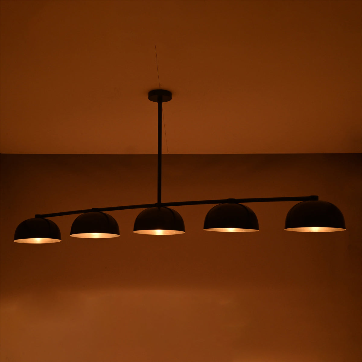 Warm glowing Orion linear chandelier with five handcrafted dome shades, highlighting soft ambient illumination in a dark interior.