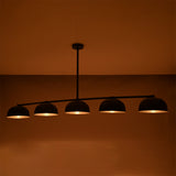 Warm glowing Orion linear chandelier with five handcrafted dome shades, highlighting soft ambient illumination in a dark interior.