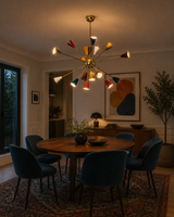 Orion 18-light multicolor Sputnik chandelier installed above a modern dining table, featuring colorful cone shades, polished brass center, and Mid-Century Modern starburst design.
