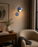 Blue Oslo dome wall sconce illuminated in a cozy modern reading corner with warm ambient lighting.