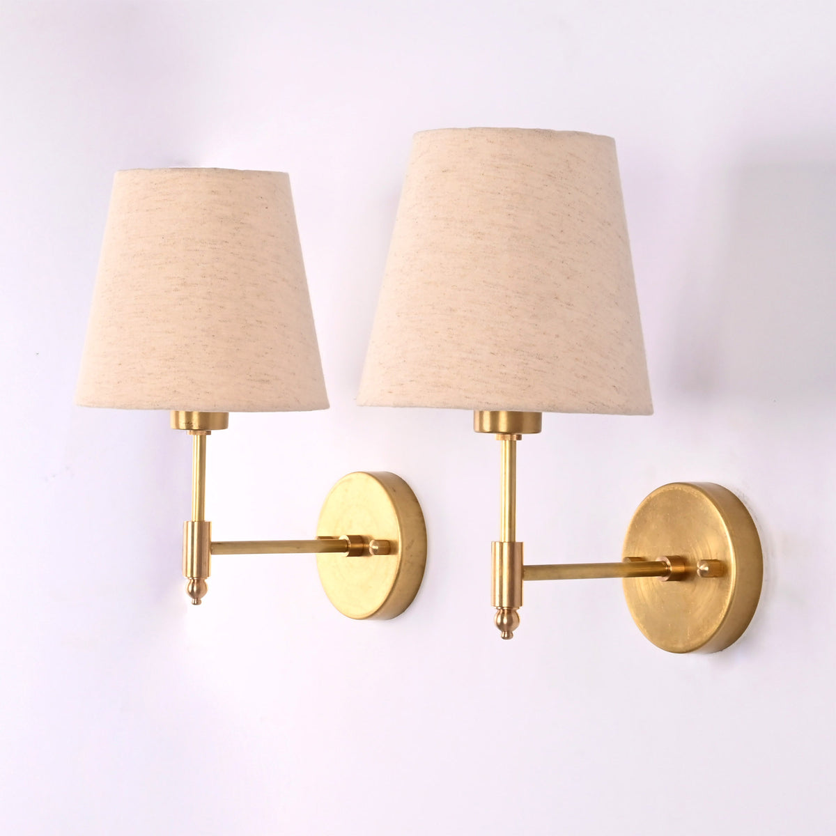 Pair of Milan brushed brass wall sconces with natural linen tapered fabric shades shown from an angled side perspective.