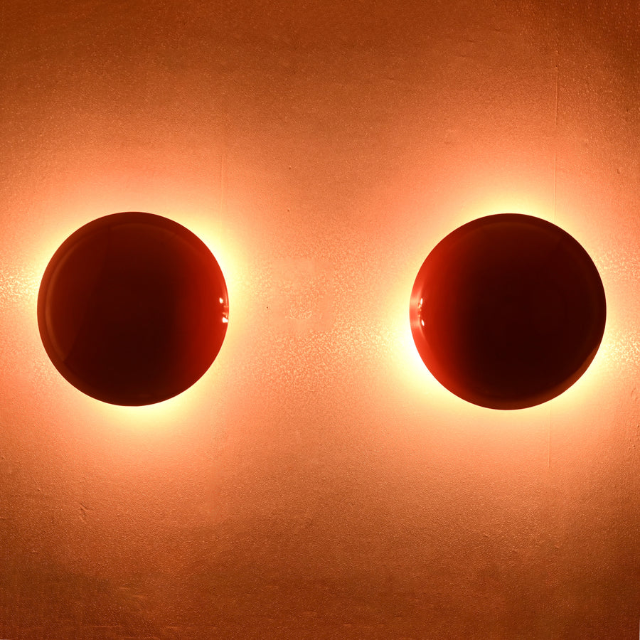 Set of two red disc wall sconces glowing with warm ambient halo, modern eclipse-inspired brass wall lighting