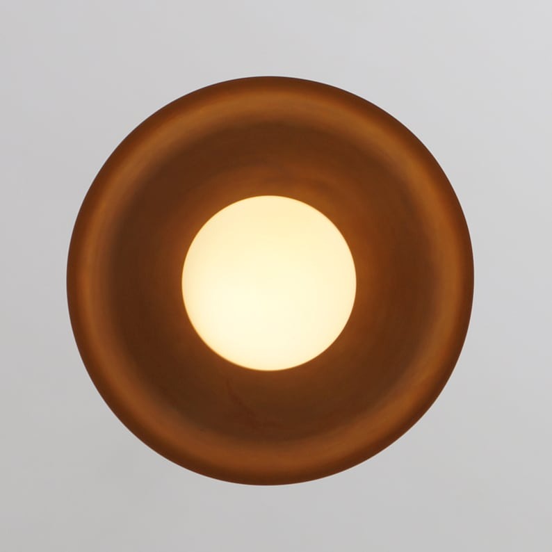 Bottom view of the Palermo 1-light pendant featuring a warm illuminated white globe centered beneath a circular bronze-tone metal dome shade.