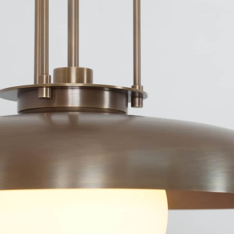 Close-up of the Palermo pendant light showcasing its brushed bronze-tone metal finish, curved dome shade, decorative suspension rods, and softly illuminated white globe.