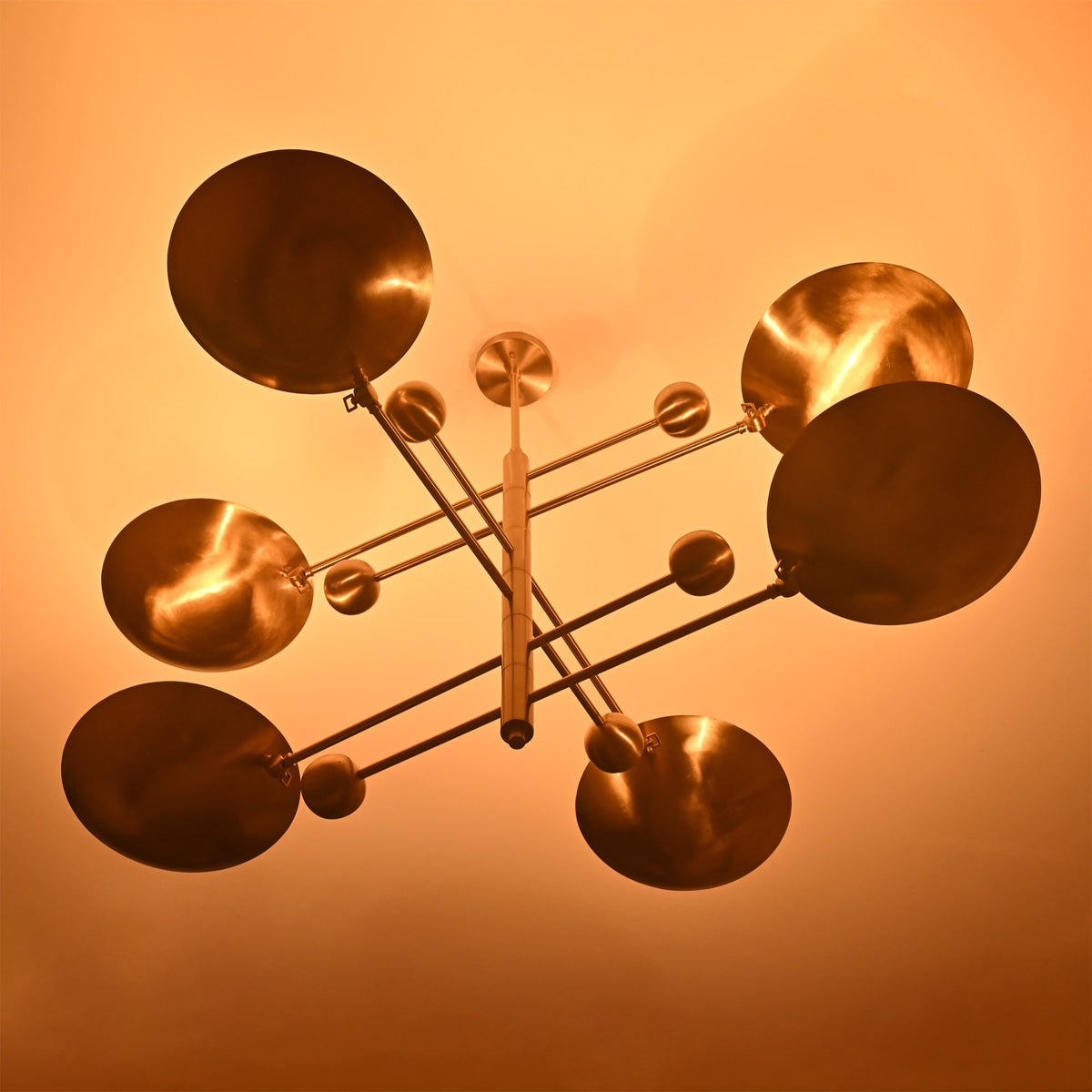 Palermo Orbital chandelier shown illuminated, casting warm light through sculptural disc shades and vertical arms.