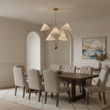 Perth 5 light sculptural chandelier shown illuminated with warm light through cream cone shades and an elegant brass-tone frame.
