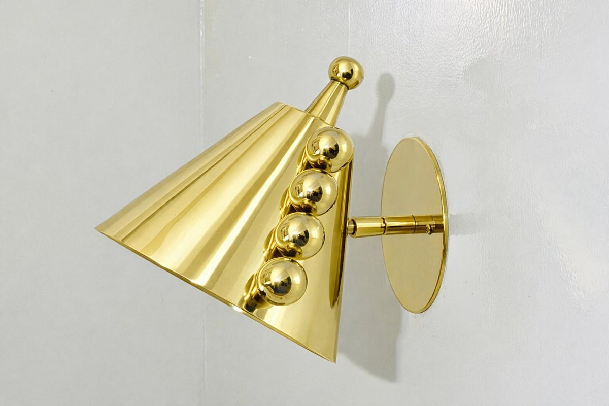 Angled view of polished brass cone wall sconce showing the round backplate, arm connection, and ball accent row.