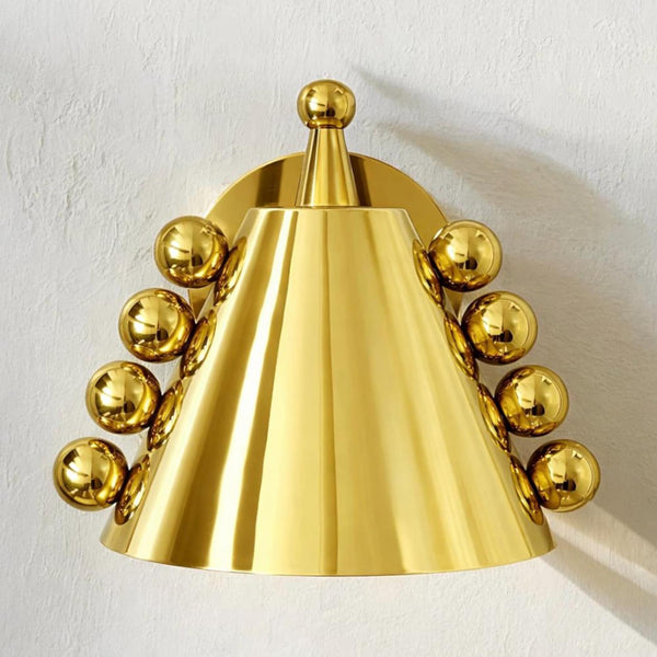 Front view of polished brass cone wall sconce with ball accents and round backplate mounted on a textured wall.