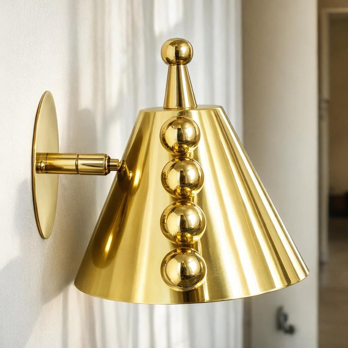 Polished brass cone wall sconce with ball accents installed on a wall in a bright interior setting.
