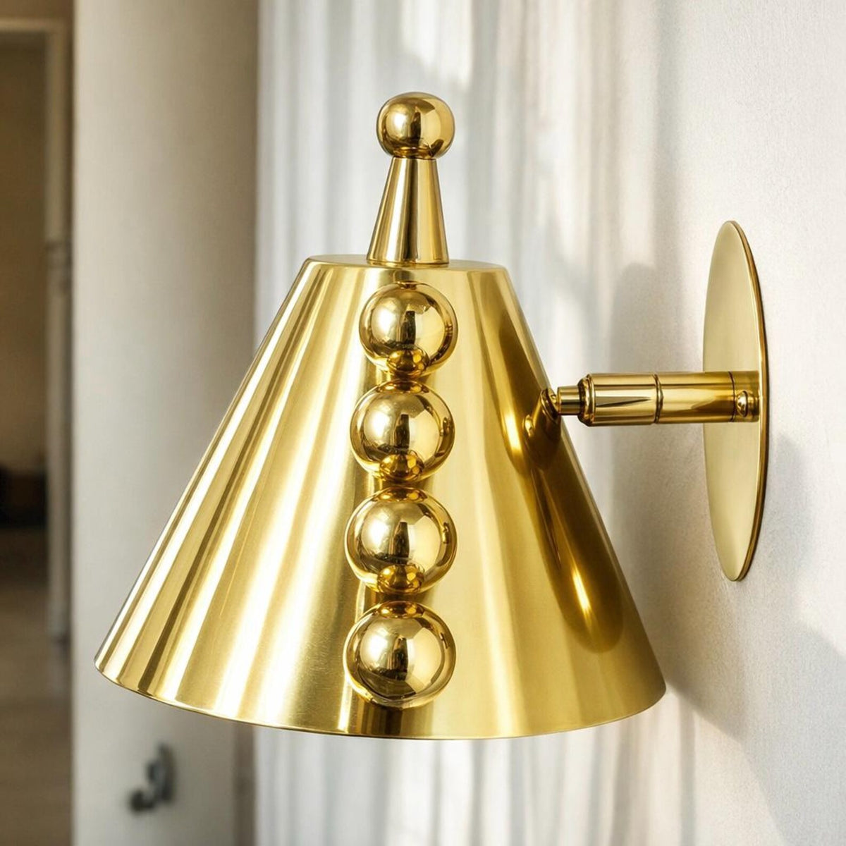 Polished brass cone wall sconce with ball accents shown from the opposite side in a softly lit interior scene.