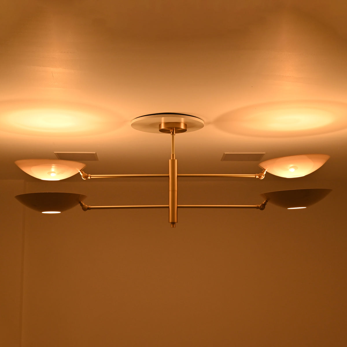 Queenstown double-tier linear chandelier with four softly illuminated ivory bowl shades and brass-tone horizontal arms in warm evening lighting.