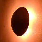 Side angled view of red circular wall lamp with radiant brass halo effect lighting