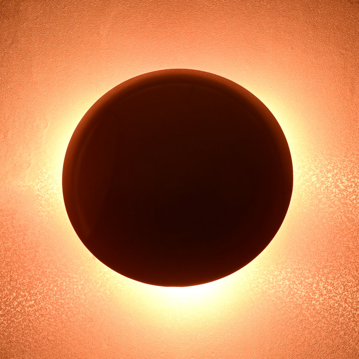 Red disc wall lamp casting warm halo light, eclipse-inspired modern wall sconce design