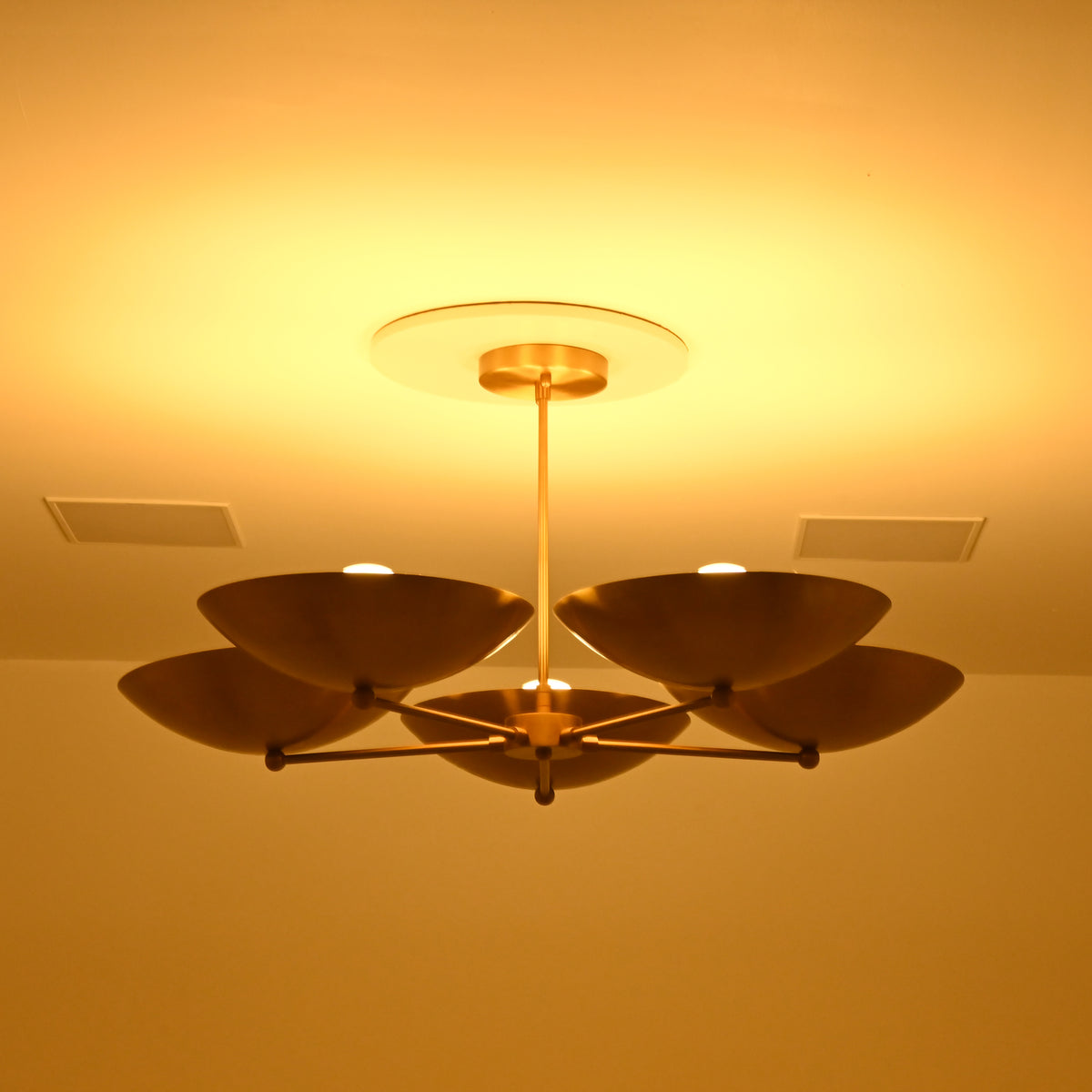  Savannah 5-light mid-century modern chandelier viewed from the side with softly illuminated bowl shades creating a warm golden atmosphere.