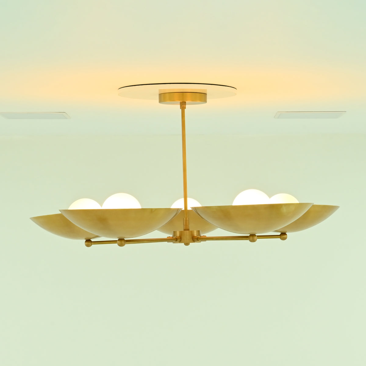 Side view of illuminated Savannah 5-light gold chandelier with upward-facing metal bowl shades and warm light reflecting across the brass finish.