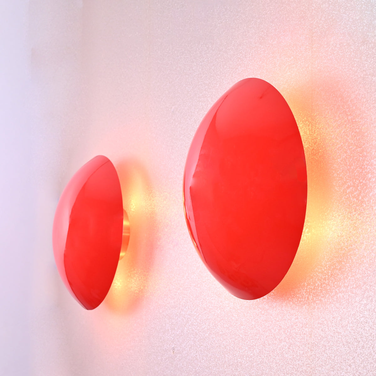 Angled side view of two red circular wall sconces glowing softly with eclipse-inspired halo ambient lighting