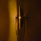 Slim side profile view of brass wall sconce illuminated in low light, highlighting circular glow effect