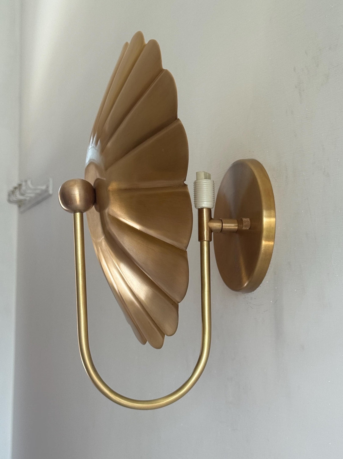 Side profile of brass flower wall sconce showing deep petal-shaped disc and U-shaped curved arm with bulb holder.