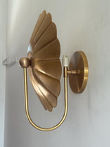 Side profile of brass flower wall sconce showing deep petal-shaped disc and U-shaped curved arm with bulb holder.