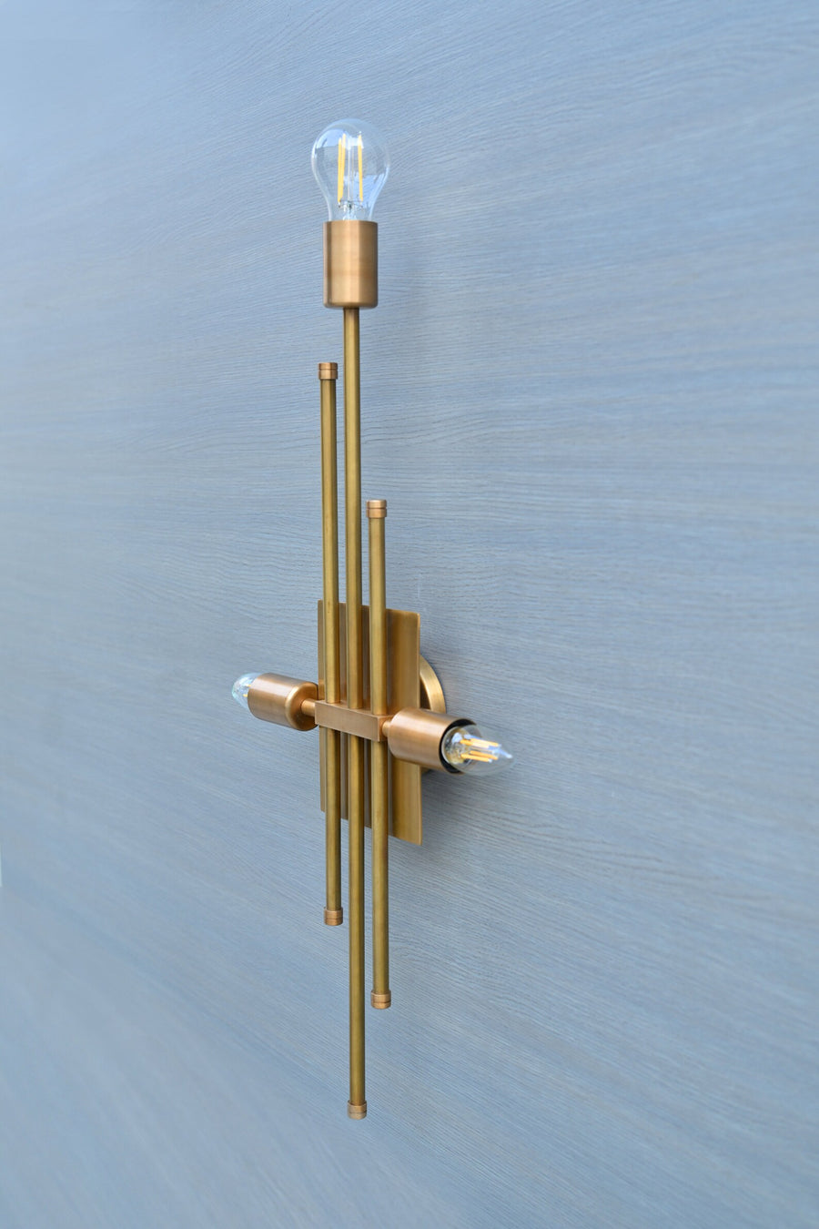 Handmade brass wall sconce featuring a vertical rod design with three light holders, modern industrial style by Brass Leaf Studio.