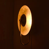 Handmade brass wall sconce glowing in dark interior, side angled view showing bowl-shaped shade lighting effect