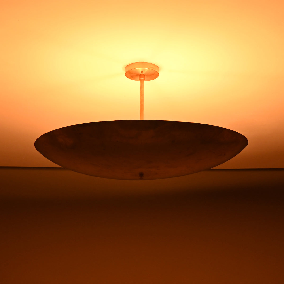 Siena Single Disc Chandelier close-up with glowing ceiling effect and dramatic low-profile bowl silhouette.