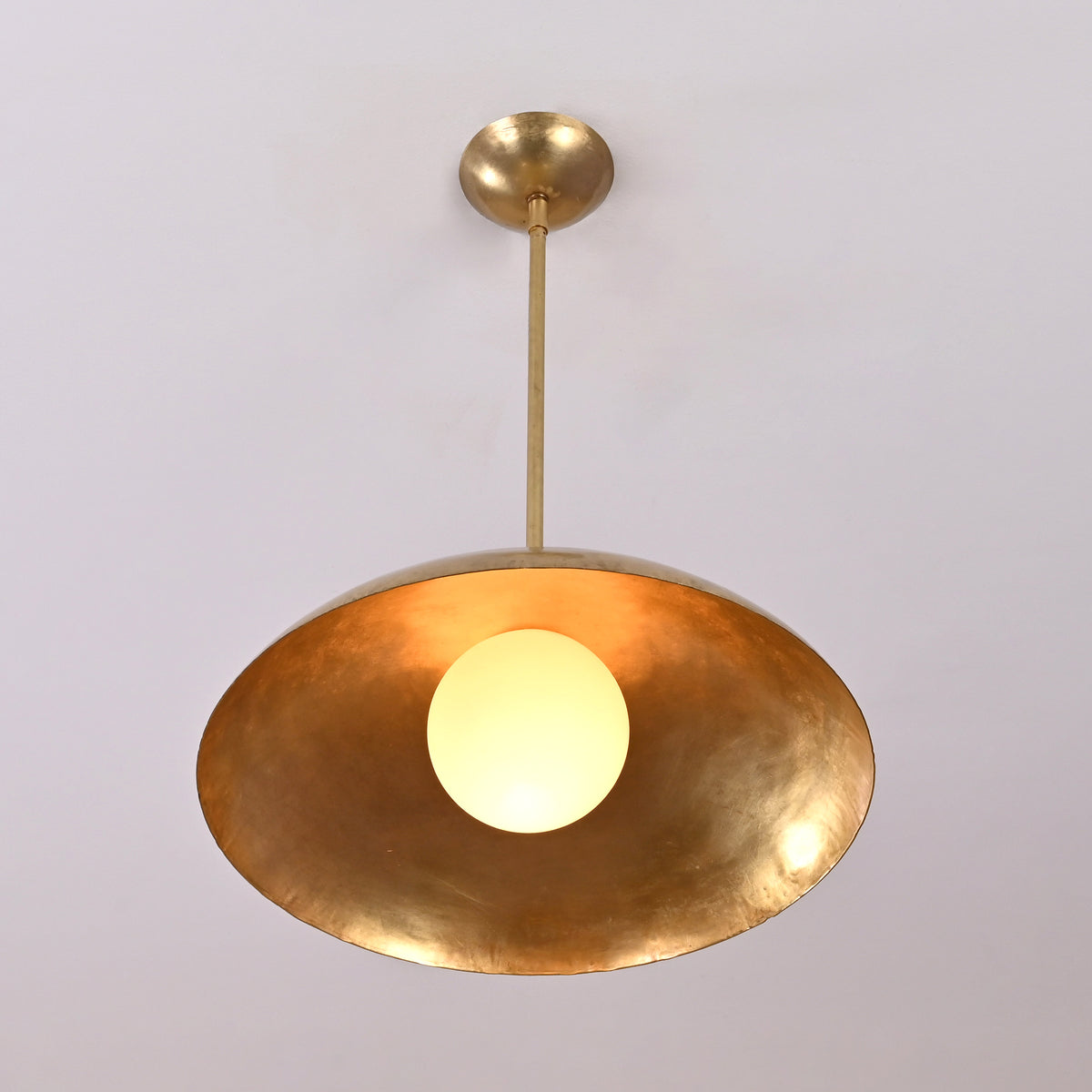 Angled view of solid brass dome pendant light with glowing bulb and lacquer-coated finish
