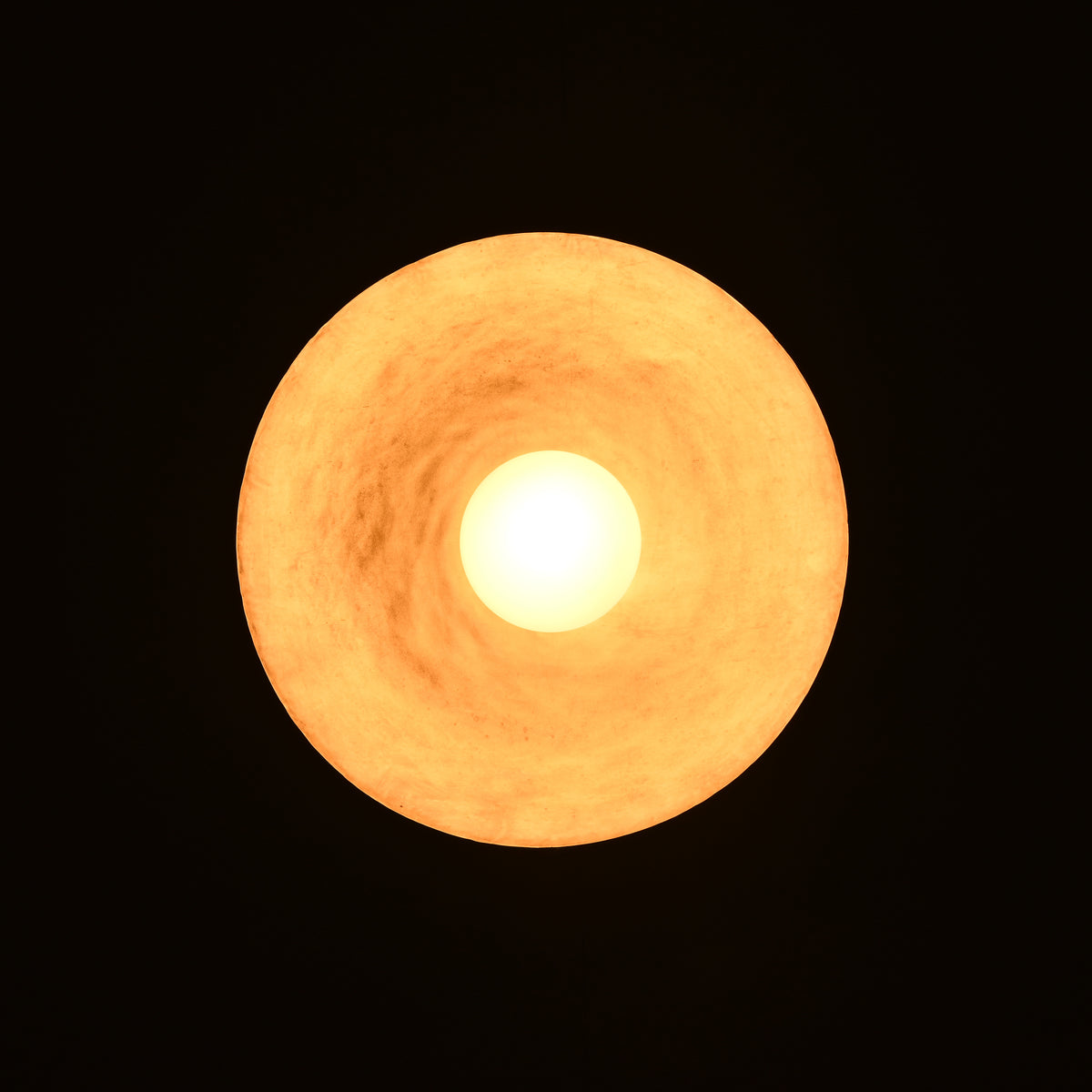 Illuminated brass pendant light viewed from below showing circular warm ambient glow