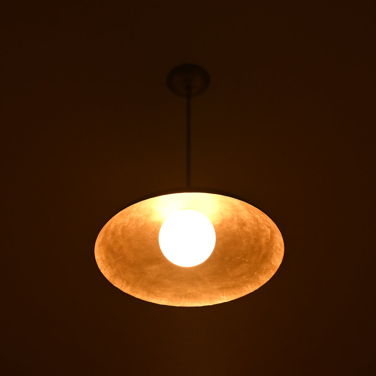 Close-up of dome brass pendant light glowing softly, handcrafted minimalist ceiling lamp