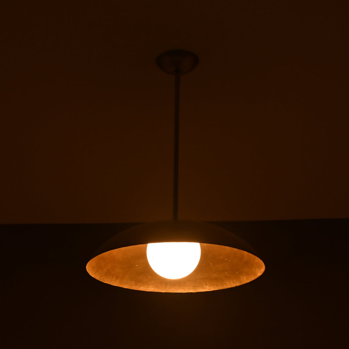 Wide view of lit brass pendant light casting ambient golden light, handmade by Brass Leaf Studio