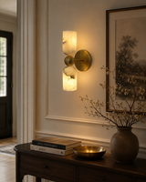Sloane Dual Alabaster Cylinder Wall Sconce installed in a sophisticated modern interior, providing warm ambient lighting above a wooden console table with elegant décor.
