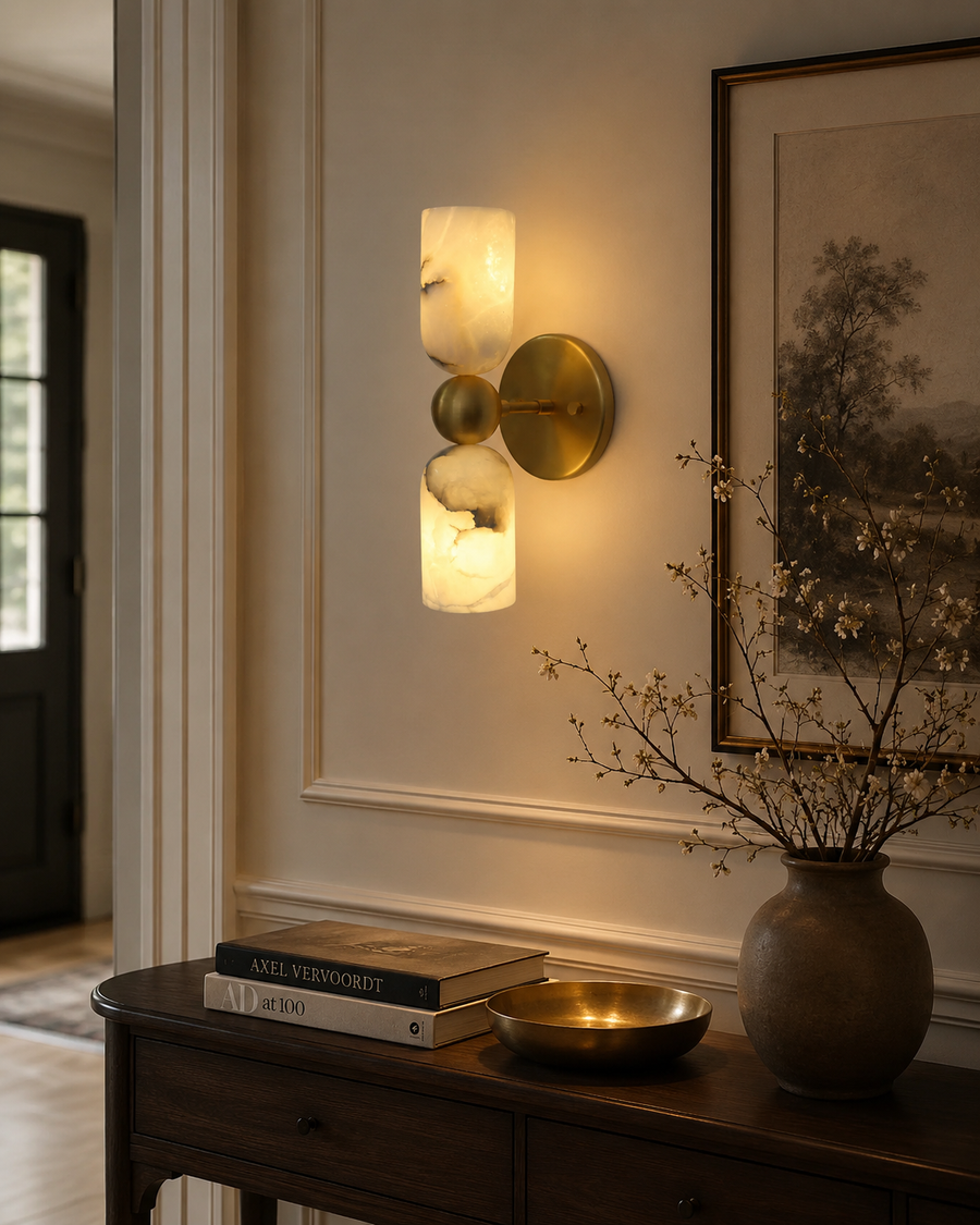 Sloane Dual Alabaster Cylinder Wall Sconce installed in a sophisticated modern interior, providing warm ambient lighting above a wooden console table with elegant décor.