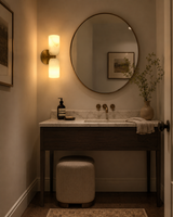 Sloane Dual Alabaster Wall Sconce installed beside a round bathroom mirror, providing warm ambient lighting in a modern luxury vanity setting.