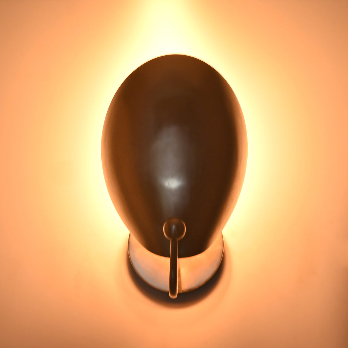 Close-up of the Sloane Modern Oval Shield Wall Sconce producing warm indirect illumination with the light source concealed behind the oversized oval shield.