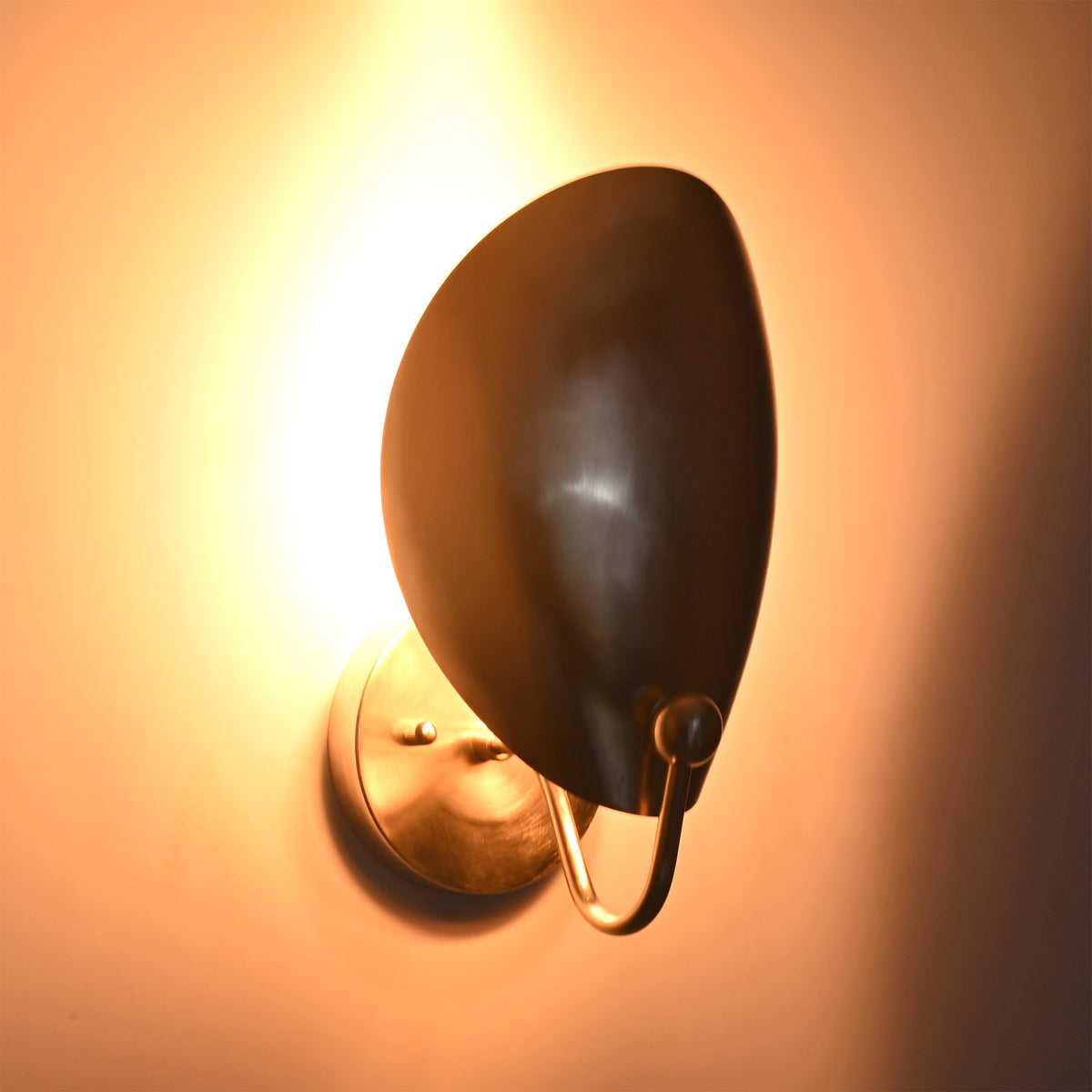 Angled illuminated view of the Sloane Modern Oval Shield Wall Sconce featuring the oversized oval shield with soft ambient backlighting and sculptural silhouette.