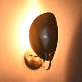 Angled illuminated view of the Sloane Modern Oval Shield Wall Sconce featuring the oversized oval shield with soft ambient backlighting and sculptural silhouette.
